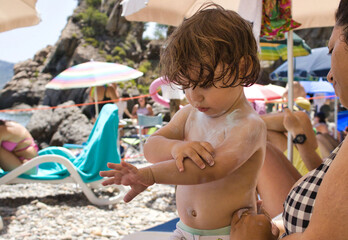 A mother and son applying suntan lotion skin protection on a crowded sandy beach in summer