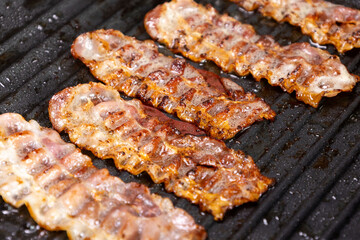 Crispy bacon strips sizzling on a hot grill in a kitchen setting during breakfast preparation