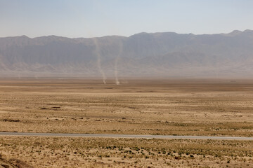 Dust devils in the vast desert of Balkh Province, Afghanistan with a road and mountains
