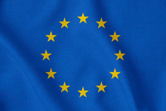 blue flag of the European Union with twelve gold stars arranged in a circle on a rough canvas with folds