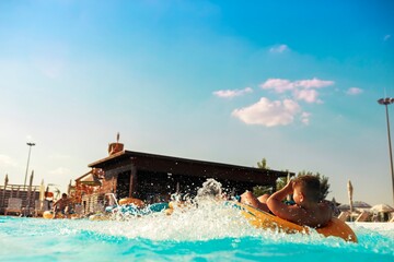A young boy relaxes on a bright yellow inflatable tube in a pool, surrounded by splashes of water....