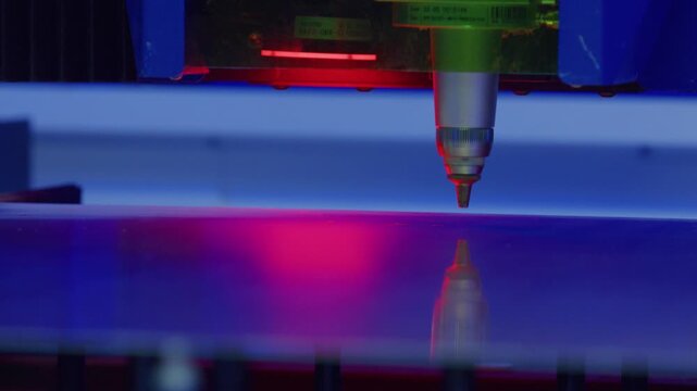Automated industrial laser engraving machine precisely etching a design onto a glass surface, illuminated by red and blue lights, showcasing advanced manufacturing technology