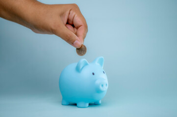 A hand is dropping coins into a piggy bank. The concept of saving and investing.