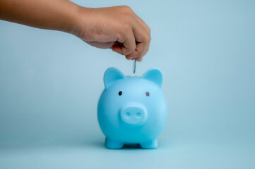 A hand is dropping coins into a piggy bank. The concept of saving and investing.