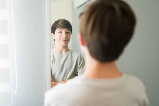 Confident teenager looking at his reflection in bedroom mirror