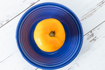 Yellow tomato on blue plate. distressed white-washed wood surface