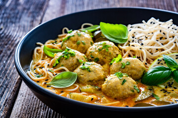 Curry soup with meatballs and zucchini with Asian noodles on wooden background	