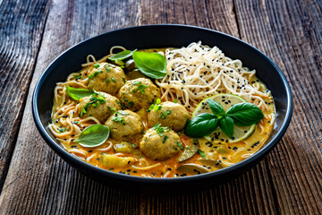 Curry soup with meatballs and zucchini with Asian noodles on wooden background	
