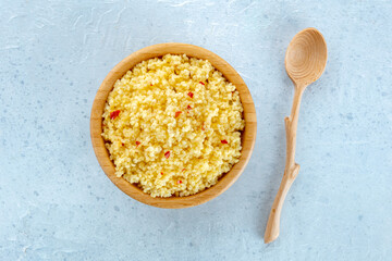 Cooked millet in a wooden bowl on a blue background, with a spoon, overhead flat lay shot. Healthy...