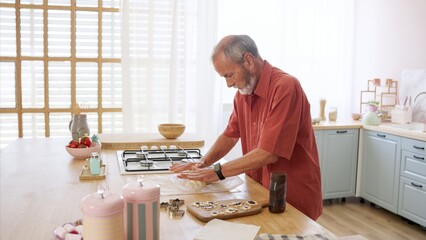 Senior man kneading dough, making cookies in kitchen