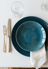 Elegant table setting with teal plates and embroidered napkin.