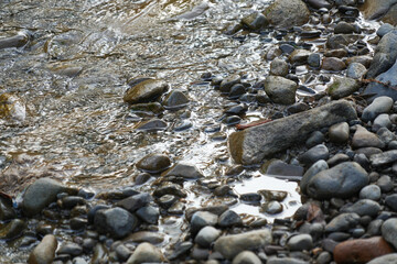 View of a stream flowing over a collection of natural stones and gravel.