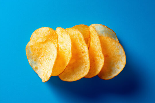A minimalist food photo featuring golden, crispy potato chips arranged neatly against a vibrant blue background.