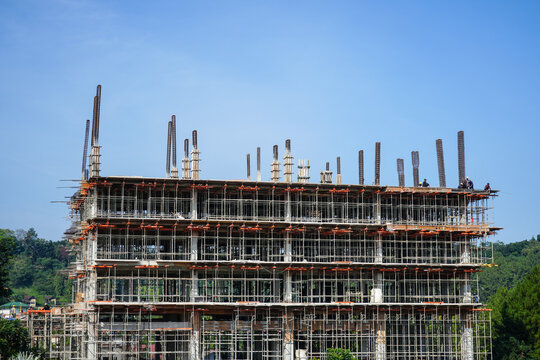 A multi-story building under construction with a clear blue sky background. The scene showcases the intricate scaffolding and steel rebars on the top floor.