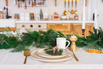 Christmas decor. Beautifully arranged dining table, elegant white plates, golden cutlery and spruce garland on white tablecloth, creating festive holiday atmosphere for meal with family and friends.