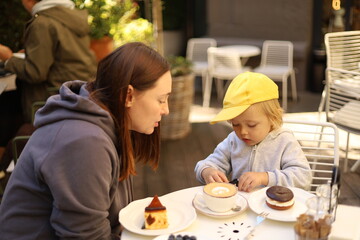 Woman with her three-year-old son sitting at a table with cakes in an outdoor cafe