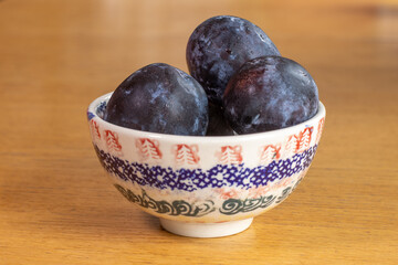 Organic plums are in the bowl on the wooden table.