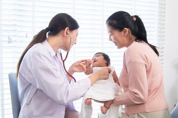 Obraz premium Asian newborn baby with mother during pediatric checkup, Close-up of pediatrician female using stethoscope on newborn baby, expressing medical care, doctor visit, family connection in child healthcare