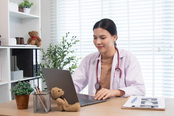 Portrait of Caucasian pediatric doctor working at desk using laptop with teddy bear reflecting child healthcare consultation service, professional clinic or modern hospital, medical occupation