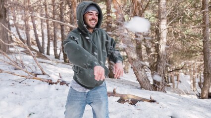 Young man throwing snowball in snowy forest