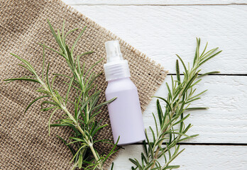 Homemade rosemary Salvia rosmarinus water made from rosemary leaves, for hair and skin care. A purple spray bottle between rosemary branches on white rustic wood board background.