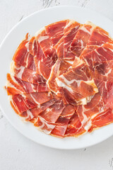 Thin Slices of Jamon Iberico Arranged on White Round Plate for Serving