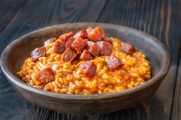 Rustic bowl of spicy tomato and chorizo risotto on wooden table