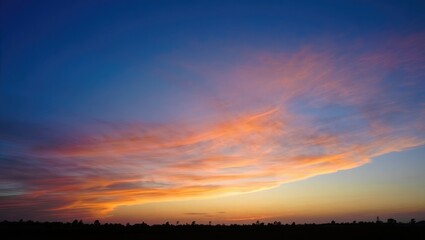 Wispy orange clouds in a blue sunset sky over dark horizon
