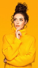Young woman with curly messy bun hairstyle wearing vibrant yellow turtleneck sweater posing thoughtfully against bright yellow background