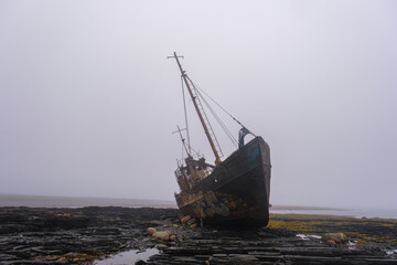 An old fishing schooner is stuck on the rocky Barents Sea, Rybachy Peninsula. The vessel is covered in rust