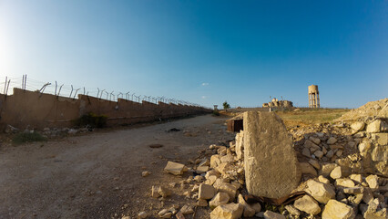 Desolate landscape with dirt road and barbed wire fence. Syria, Sednaya Prison.