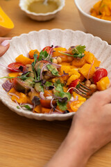 Person holding plate with autumn warm chickpea and roasted pumpkin salad with fresh cherry tomatoes