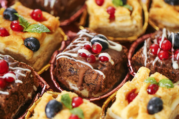 Colorful sweet desserts with fruits. Mini cakes with berries and chocolate. Festive assortment of decorated cakes. Variety of pastry with cream and toppings. Tasty selection of bakery sweets.