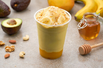 Layered Avocado and Mango Smoothie with Banana, Honey, Vanilla ice cream, and Nuts in glass side view of healthy drink
