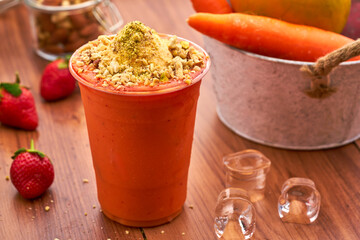 Mango Carrot Smoothie with Vanilla ice cream, Nuts, Pistachios, and a Fresh Strawberry Garnish in glass side view of healthy drink