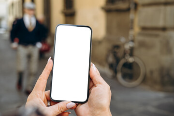 Smartphone mock up held by hands with blank screen in urban setting, showcasing modern technology and lifestyle with copy space available