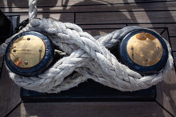 Close-up of thick rope wrapped around metal cleats on wooden deck. Strength, reliability,...