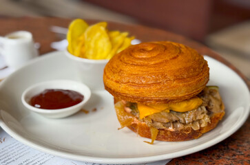 Croissant burger with side chips and ketchup served in modern cafe environment. Food, lifestyle, and gastronomy reflecting casual dining, fast cuisine and contemporary flavor experience.