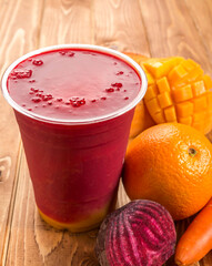 Layered Fruit and Vegetable Smoothie with Mango, Orange, Beet, and Carrot in glass on wooden table side view of fresh drink