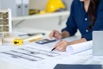 Asian adult architect meticulously designs building blueprints planning urban structures calculating project costs at modern office workspace