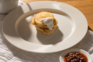 Delicious stack of pancakes topped with creamy goodness, served on a white plate alongside vibrant jam, perfect for a delightful breakfast