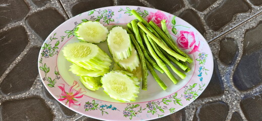 Peeled and cut cucumbers into bite-sized pieces. Yardlong bean are cut into short pieces on an oval plate. Organic vegetables are prepared and served with the meal. Side dishes or Appetizers in table
