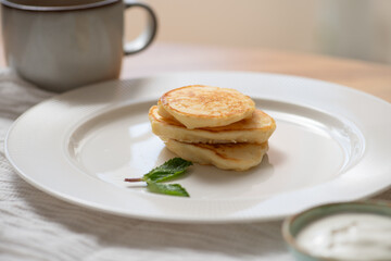 Small stack of golden brown pancakes, beautifully garnished with fresh mint, resting on a white plate, inviting for a delightful breakfast