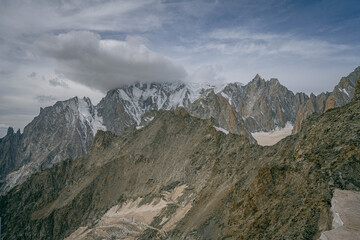 Fototapeta premium Rugged alpine peaks of the Alps with dramatic rocky ridges and snowy summits under cloudy sky showing wild mountain landscape