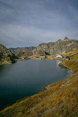 Alpine lake in the mountains surrounded by rocky peaks and grassy slopes with small houses on the shore under clear sky creating peaceful scenery