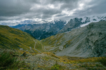 Fototapeta premium Panoramic view of Stelvio Pass mountain pass with legendary hairpin bends climbing steep alpine slopes toward rocky ridges under sky