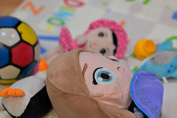 Colorful children's toys, including a multicolored soccer ball and plush dolls, are scattered on a baby mat. The mat features playful designs and letter.