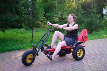 Woman riding a pedal kart recreational vehicle on a paved path in a park on a sunny day. Summer activity.