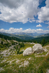Dolomites alpine meadow with rocky boulders in foreground and panoramic mountain range under blue summer sky with clouds scenic landscape