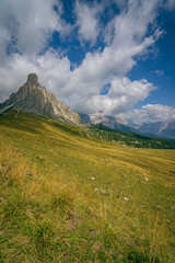 Passo Giau in the Dolomites with Ra Gusela mountain peak rising above alpine meadow under partly cloudy blue summer sky